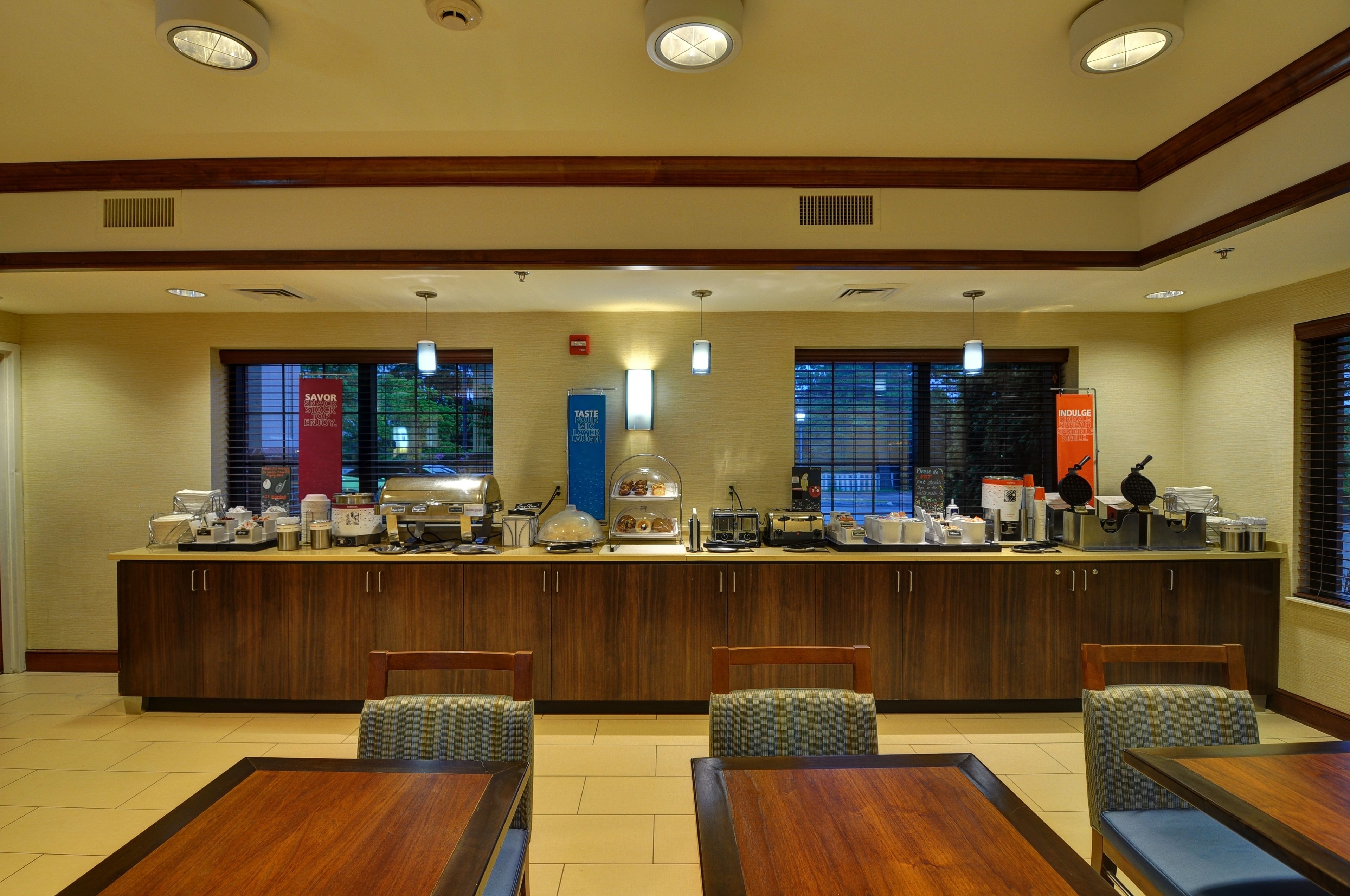 A hotel breakfast area with a counter, seating, and various breakfast items.