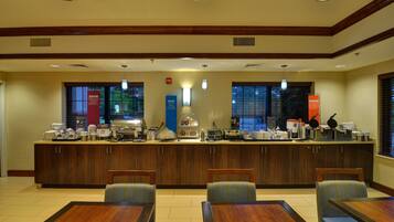 A hotel breakfast area with a counter, seating, and various breakfast items.