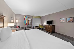 A hotel room with a large bed, a desk, a chair, a dresser, a television, and two framed pictures on the wall.