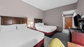 A hotel room with two beds, a desk with a television, a lamp, and a door leading to another room.
