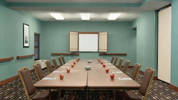 A conference room with a long table, chairs, a projector screen, and a patterned carpet.