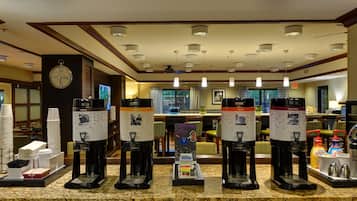 A coffee station with multiple coffee makers and a clock on the wall.
