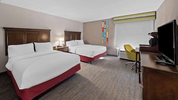 A hotel room with two beds, a desk with a TV, a chair, and a colorful artwork on the wall.