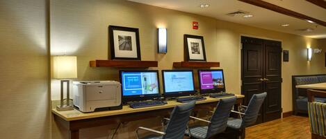 A hotel reception area with a desk, computers, chairs, and framed pictures on the wall.