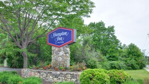 Ein Schild des Hampton Inn by Hilton an einem Steinsäule mit einem Garten davor.