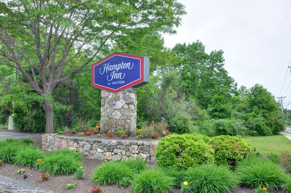 A Hampton Inn by Hilton sign on a stone pillar with a garden in front. - Hampton Inn Franklin/Milford (Franklin)