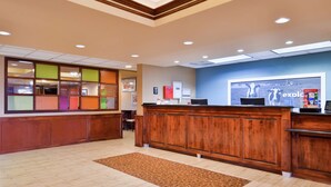 A reception area with a wooden reception desk, a large framed artwork, and a patterned rug. - Hampton Inn Greensboro-East (McLeansville)