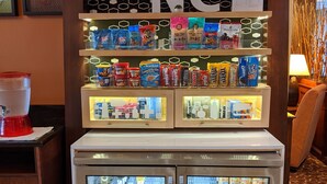 A snack display with various packaged foods and a True refrigeration unit with beverages. - Hampton Inn Greensboro-East (McLeansville)