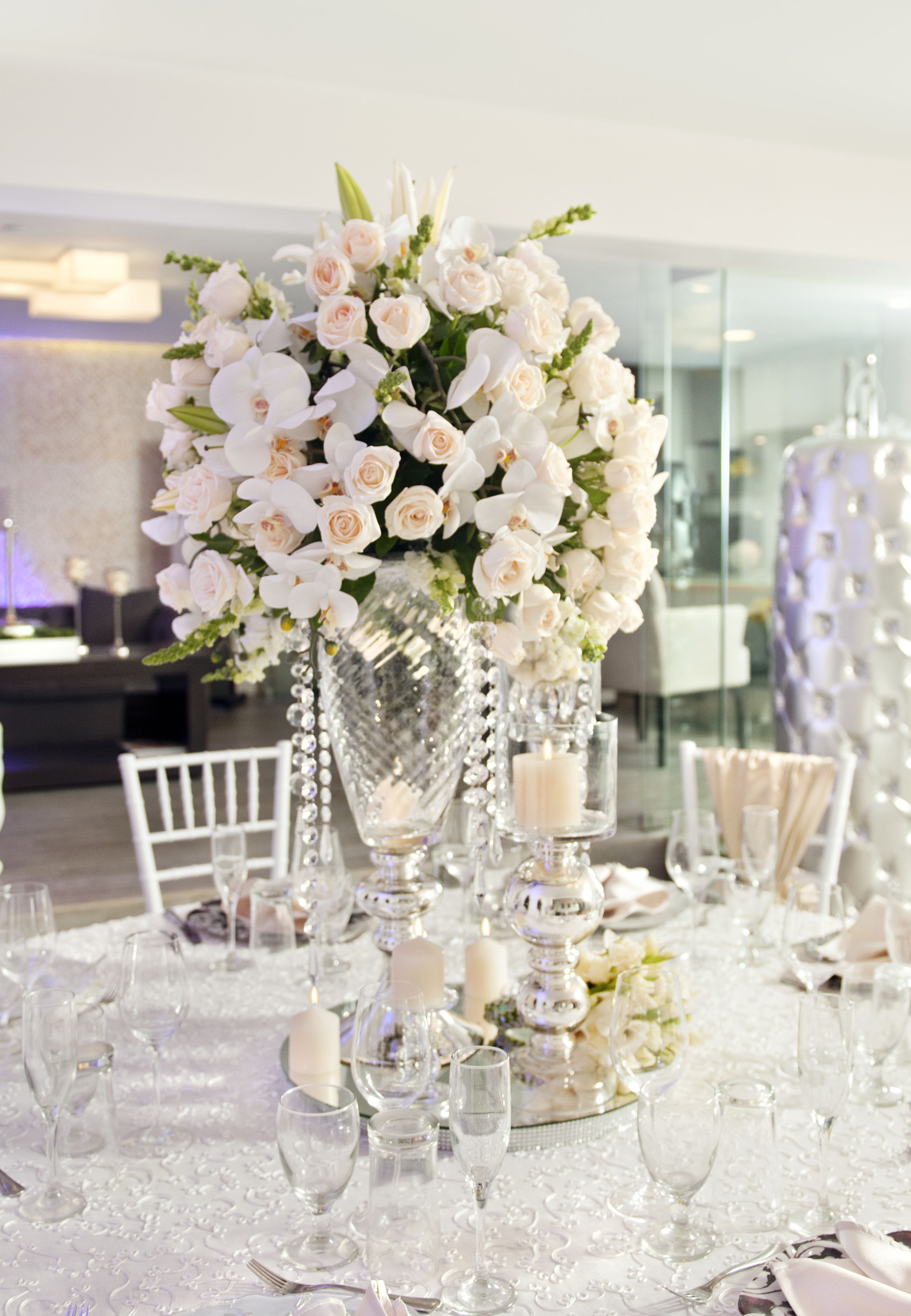 Una mesa dispuesta para un evento formal con flores blancas, velas y cristalería transparente.
