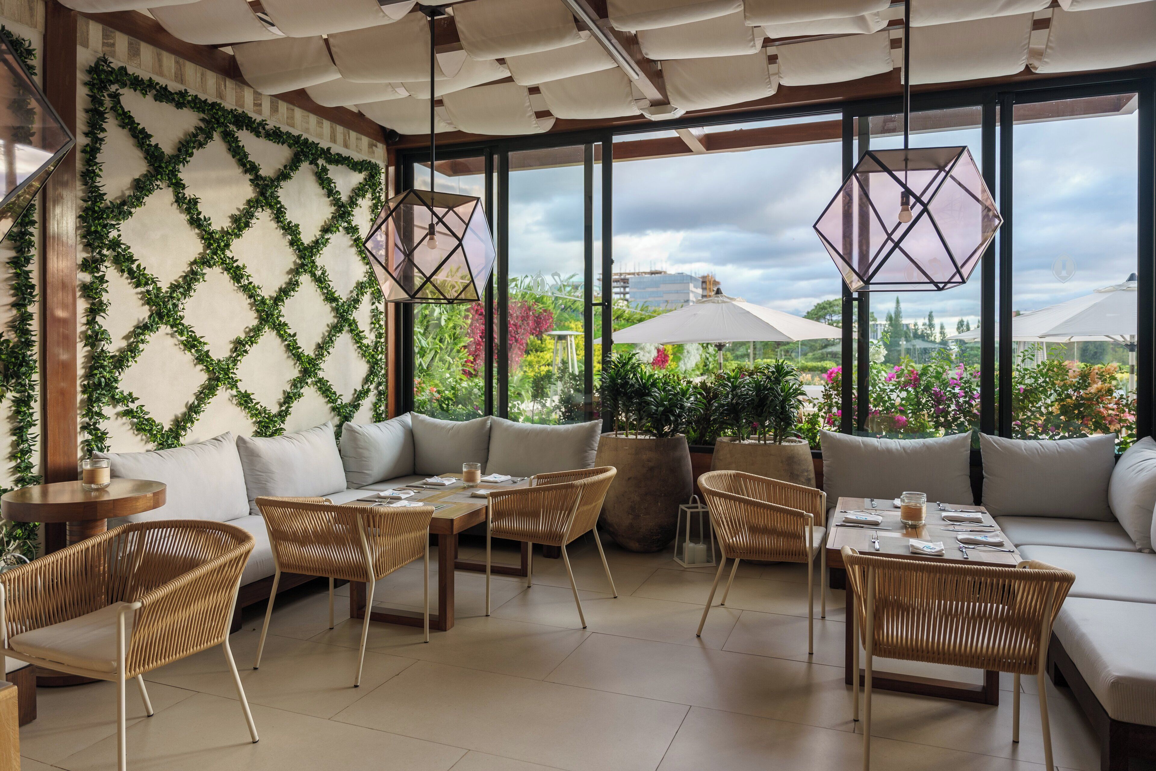 Un área de estar moderna al aire libre con mobiliario de mimbre, un sofá acolchado y vistas a un jardín a través de amplias ventanas.