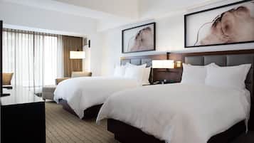 A hotel room with two beds, a desk, and a chair. There are two framed pictures on the wall.