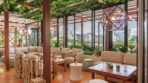Un rincón interior acogedor con sillas y mesas acolchadas, rodeado de amplios ventanales con vistas a la ciudad.