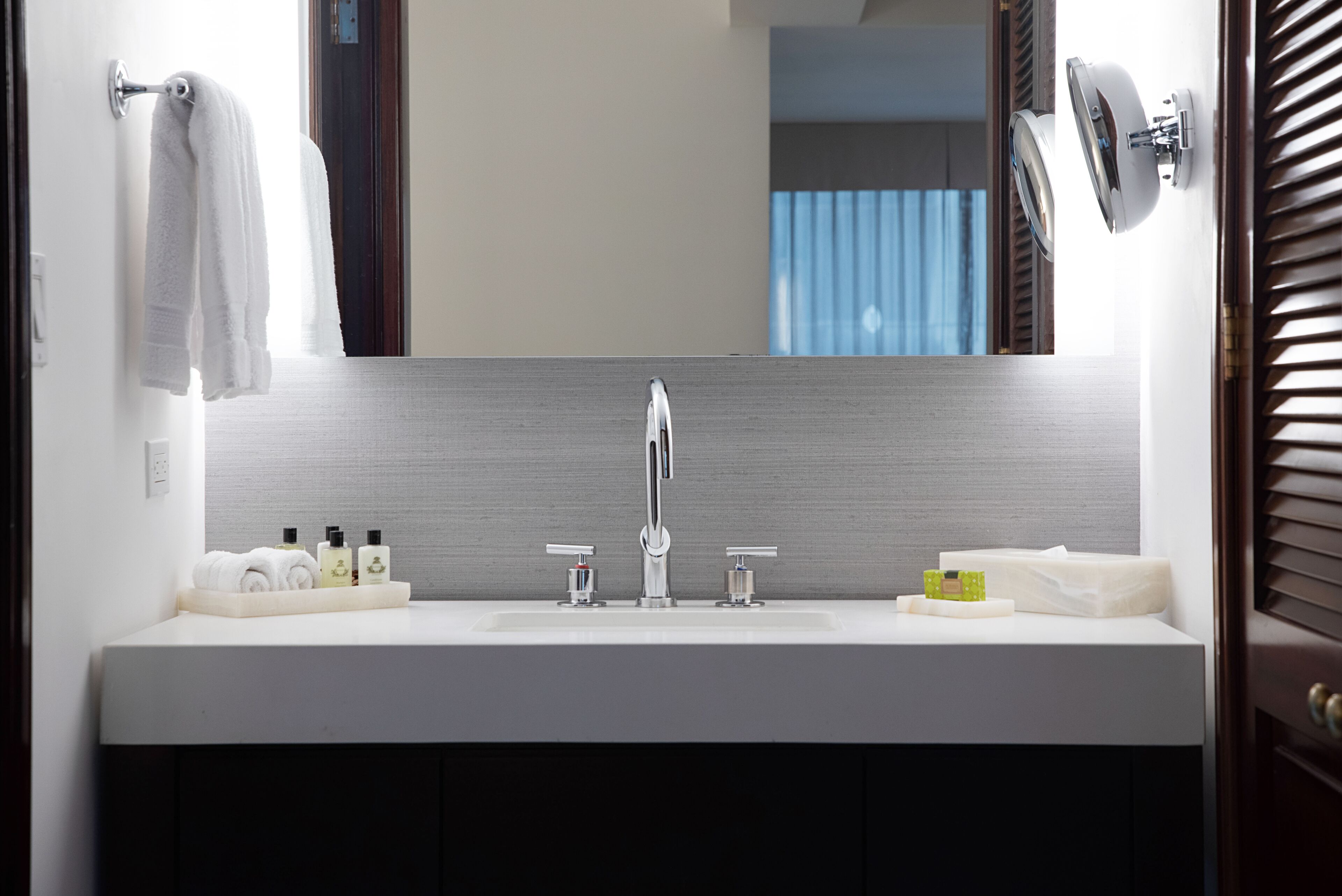 Un baño moderno con un espejo grande, un lavabo blanco y artículos de aseo en la encimera.