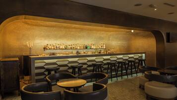 Una zona de bar con pared decorada, taburetes y mesas.
