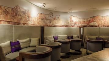 Um espaço de spa com várias áreas de estar, incluindo sofás e poltronas confortáveis, dispostas ao redor de uma mesa de massagem central.