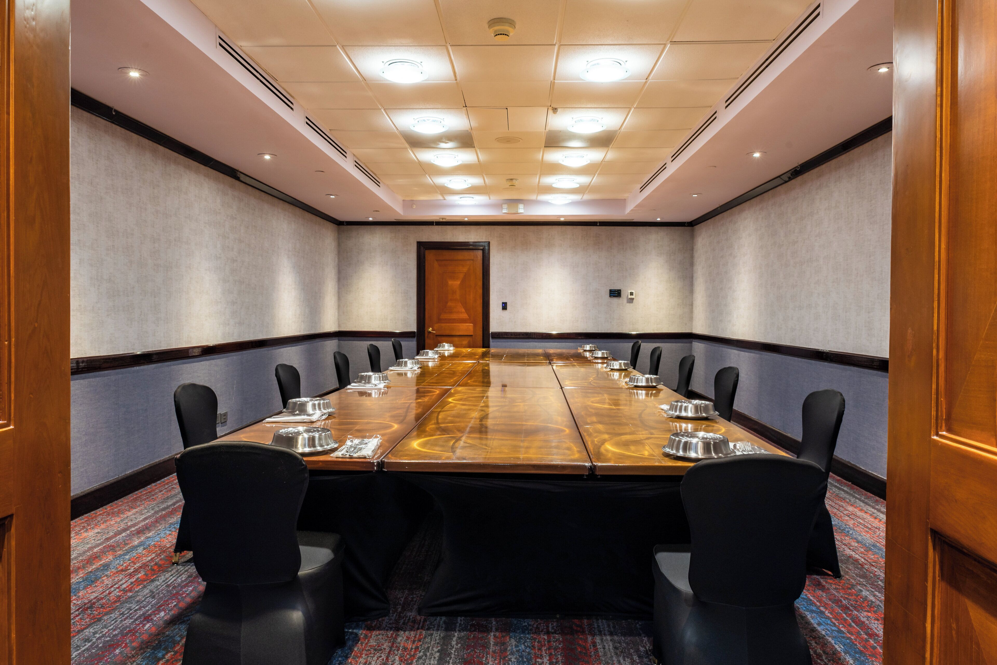 A conference room with a long table, black chairs, and a carpeted floor.