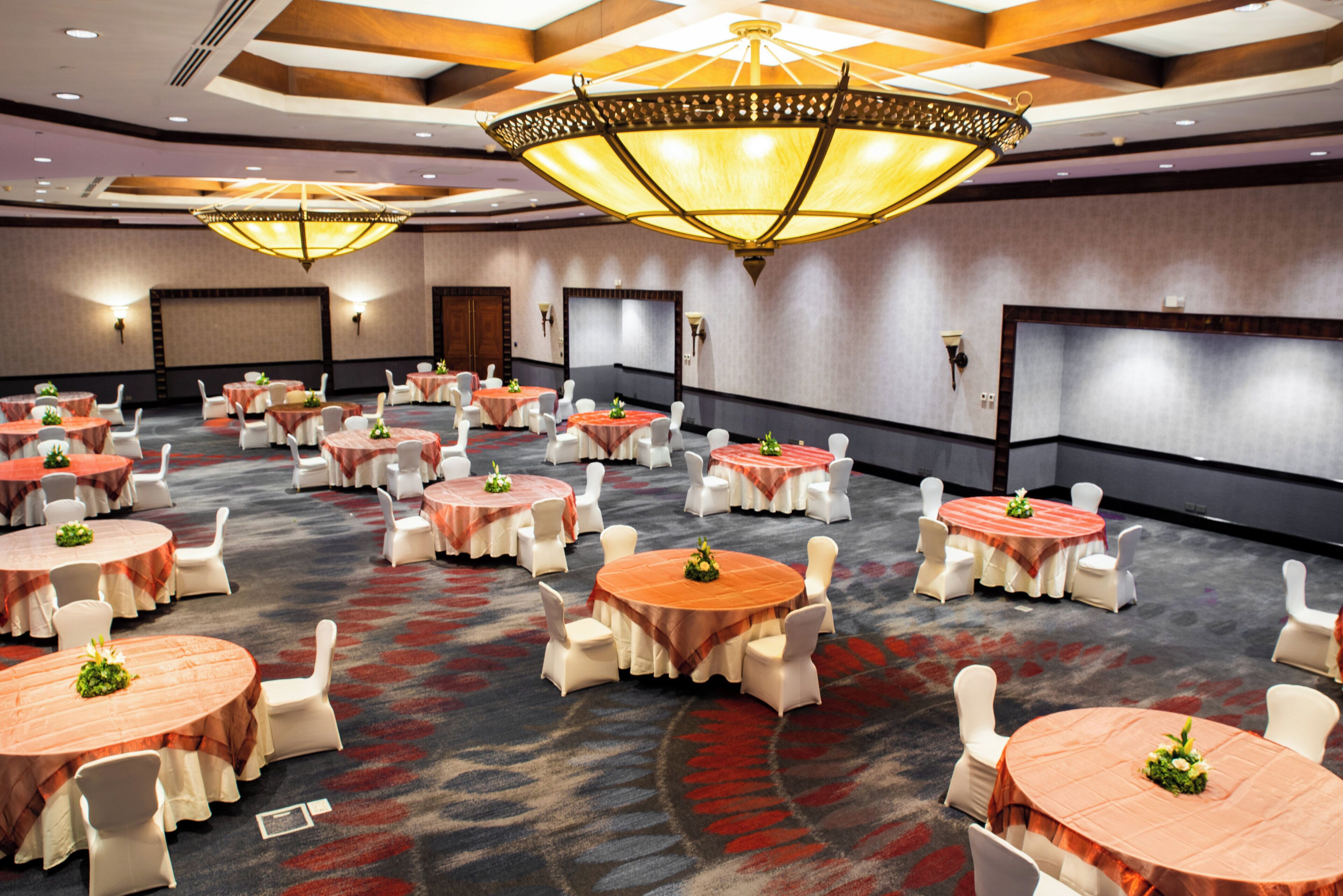 Un salón de conferencias con varias mesas redondas, sillas blancas e iluminación colgante.