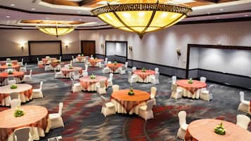 Un salón de conferencias con varias mesas redondas, sillas blancas e iluminación colgante.