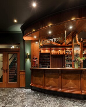 A reception area with a wooden counter, a sign that reads "RECEPTION", and a staircase leading to an upper level. - Hotel Nova Berlin (Berlin)