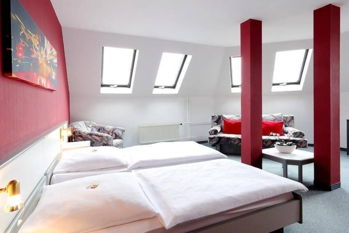 Une chambre d’hôtel avec deux lits, un canapé, une petite table et des fenêtres de toit.