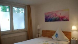 A bedroom with a bed, a nightstand, a lamp, a window with curtains, and a painting on the wall. - To Be Deleted - Hotel Princess (Rodenbach)