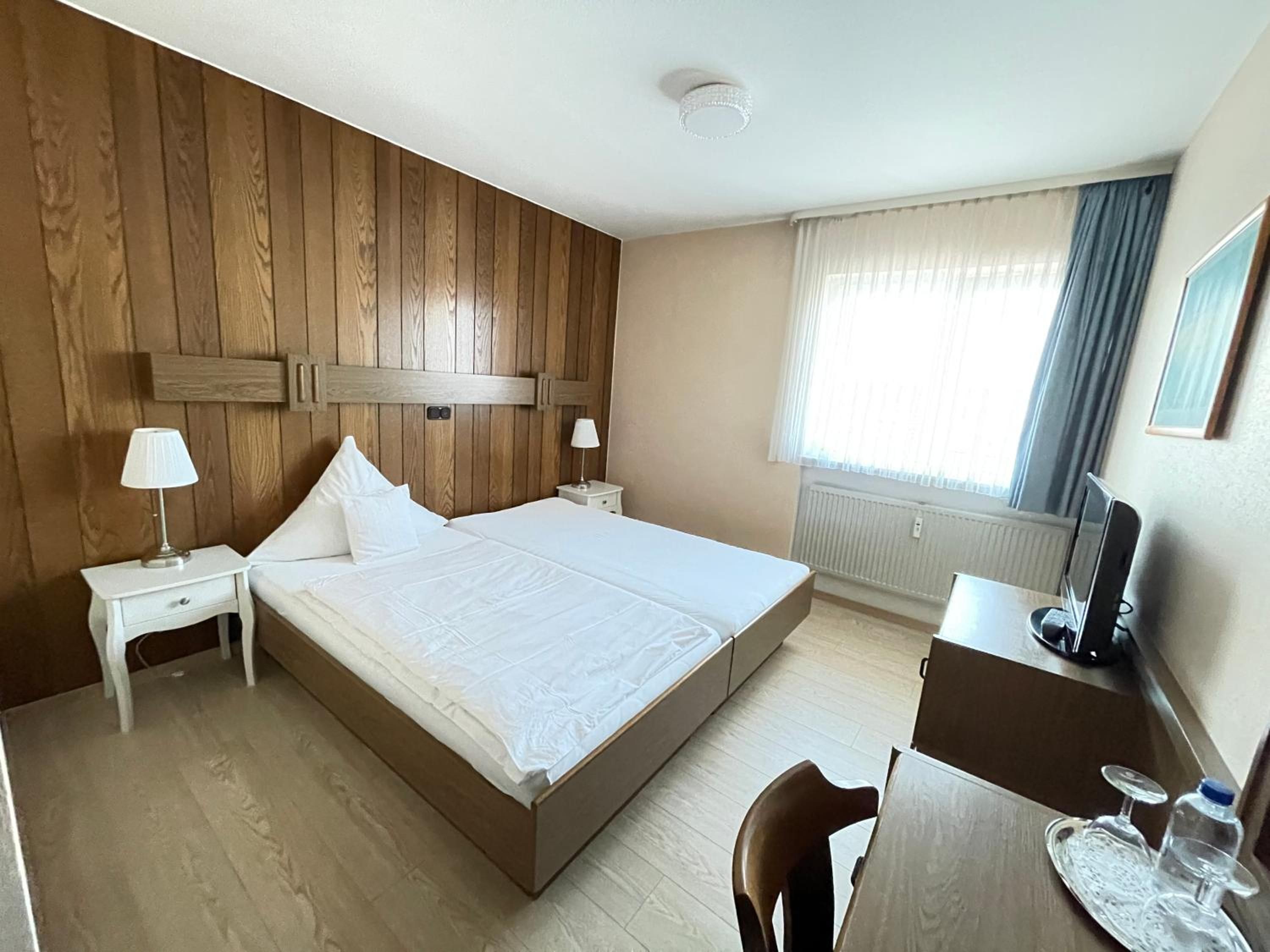 Une chambre d’hôtel avec une tête de lit en bois, un lit, un bureau avec une chaise, une lampe et un téléviseur.