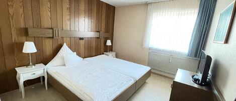 Une chambre d’hôtel avec une tête de lit en bois, un lit, un bureau avec une chaise, une lampe et un téléviseur.