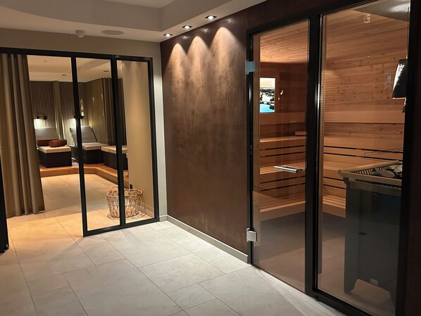 Una habitación de hotel moderna con una puerta corrediza de vidrio que da a un balcón, una zona de estar con cojines y una sauna de madera.