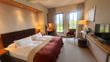 A hotel room with a large bed, a desk with a television, a chair, and a window with a view of the outdoors.