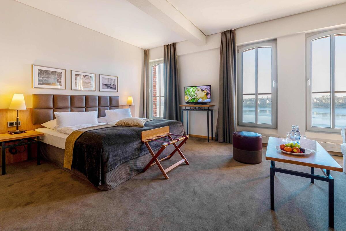 Een hotelkamer met een bed, een televisie, een tafel met fruit en uitzicht op de stad.