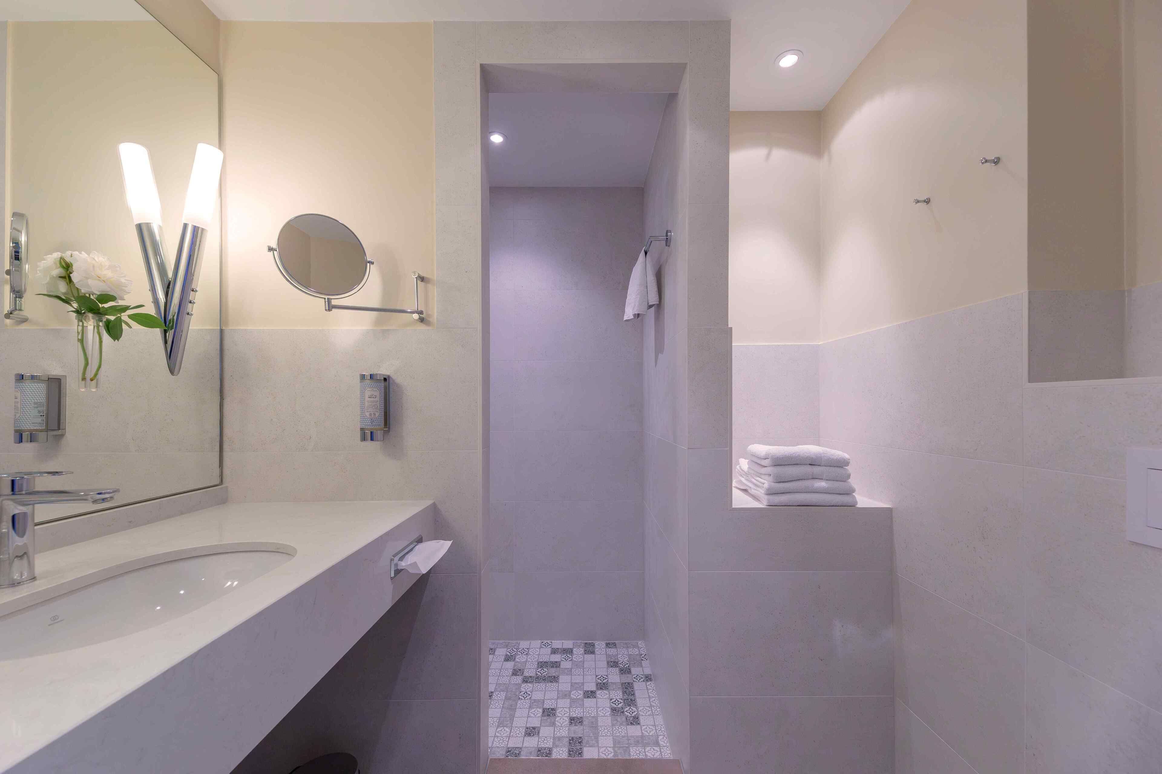 A modern bathroom with a large mirror, a sink, and a shower area.