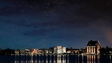 Una vista nocturna de un frente marítimo con edificios reflejándose en aguas tranquilas.