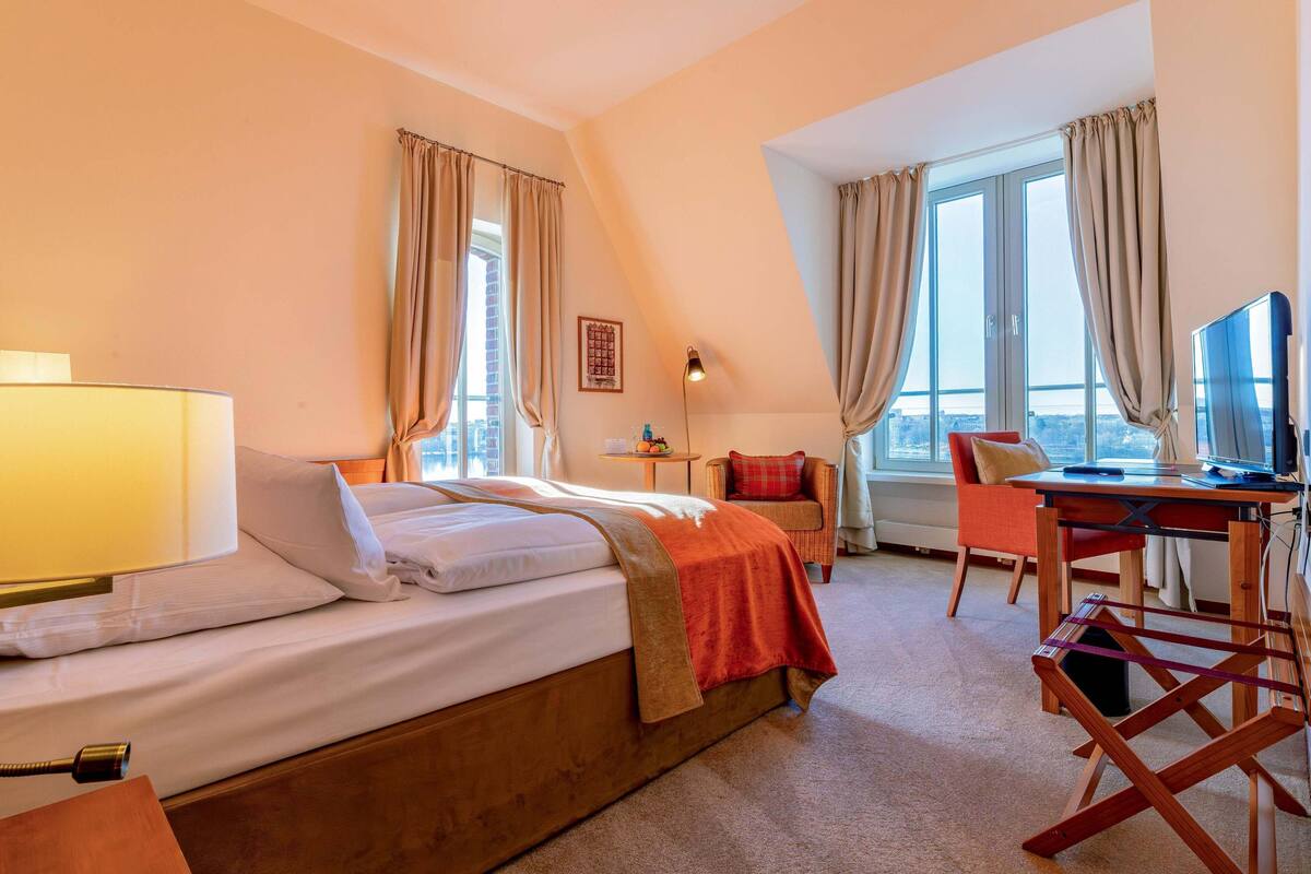 Hotelkamer met een bed, een bureau, een stoel, een lamp en een raam met gordijnen.