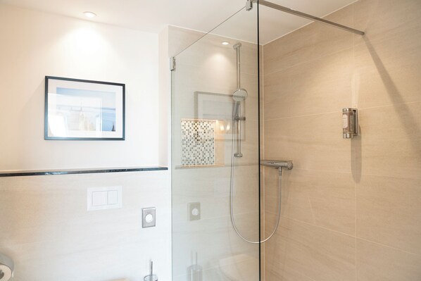 Un baño moderno con ducha envuelta en vidrio, un cuadro en la pared y un salpicadero de azulejos.