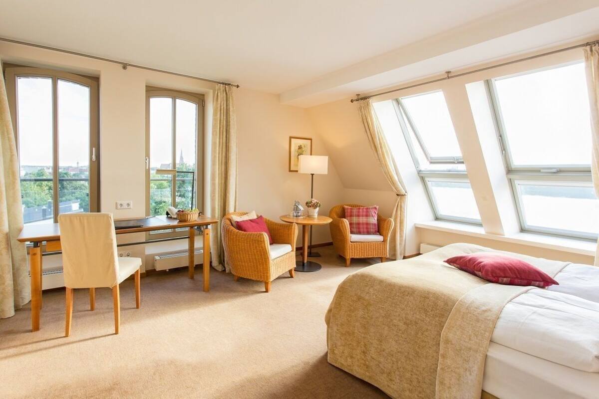 Een hotelkamer met een bed, bureau, twee stoelen, een kleine tafel en grote ramen.