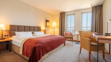A hotel room with a large bed, two bedside lamps, a chair, a desk, and a window with curtains.