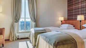 Habitación de hotel con dos camas, vista a la ciudad a través de un ventanal grande, pared con estampado escocés y dos lámparas de noche.