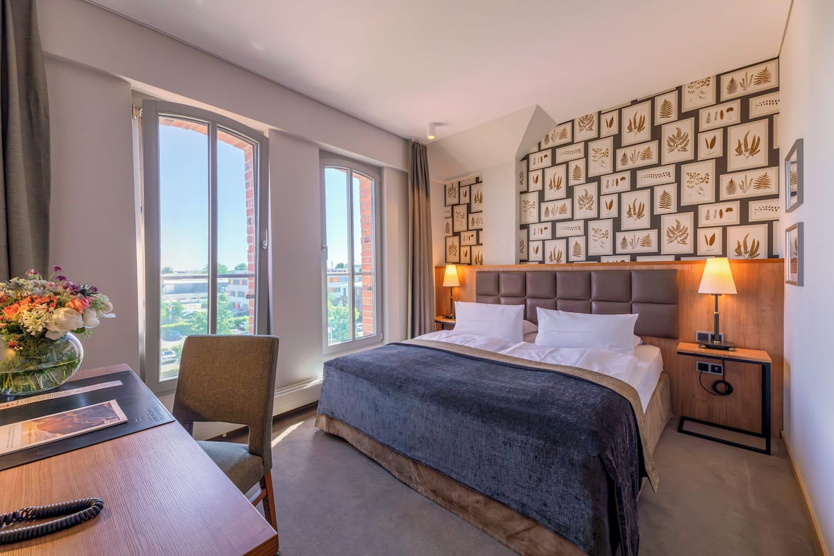 Een hotelkamer met een groot bed, een bureau met stoel, een bloevas en uitzicht op de stad.