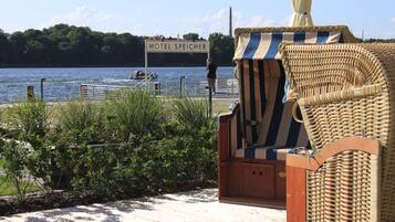 A wooden deck with a wicker chair and a sign reading "HOTEL SPEICHER" by the water.