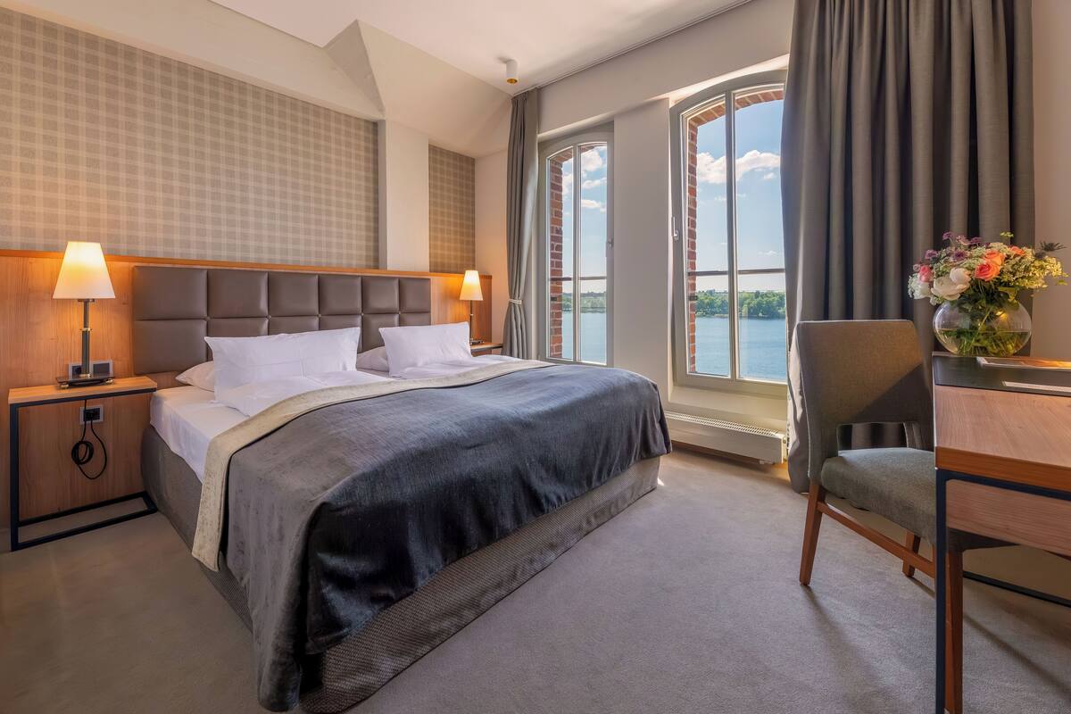 Een hotelkamer met een groot bed, een bureau en uitzicht op een waterpartij.
