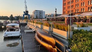 Hotel aan het water met een steiger, boten en een groot rood gebouw op de achtergrond.