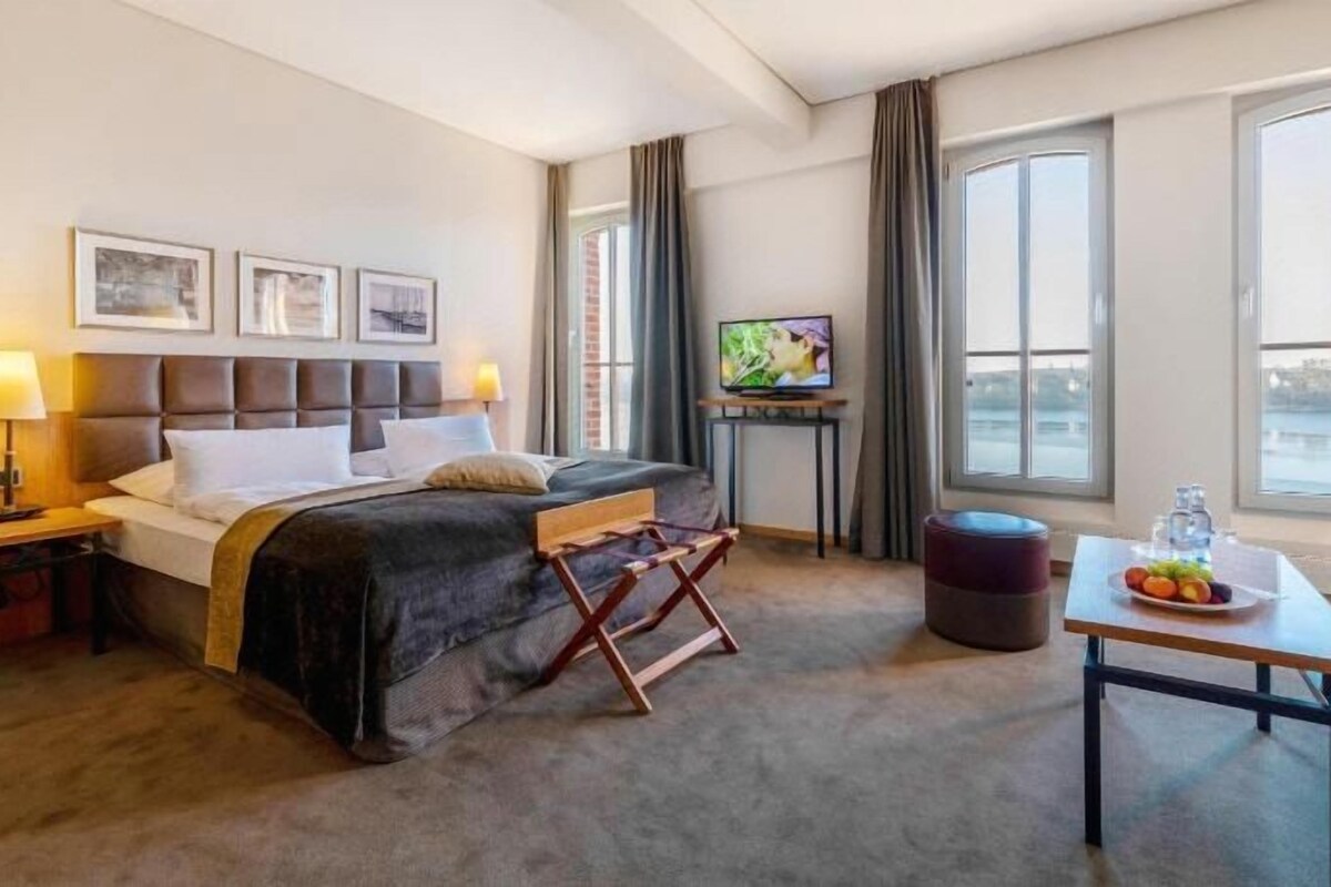 Een hotelkamer met een bed, een televisie, een tafel met fruit en uitzicht op het omliggende landschap.