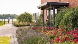Een gebouw van baksteen met een overdekte galerij en een tuin vol bloemen en struiken.
