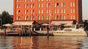 Een hotel met een gevel van baksteen, buiten zitplaatsen en een boot afgemeerd voor de deur.