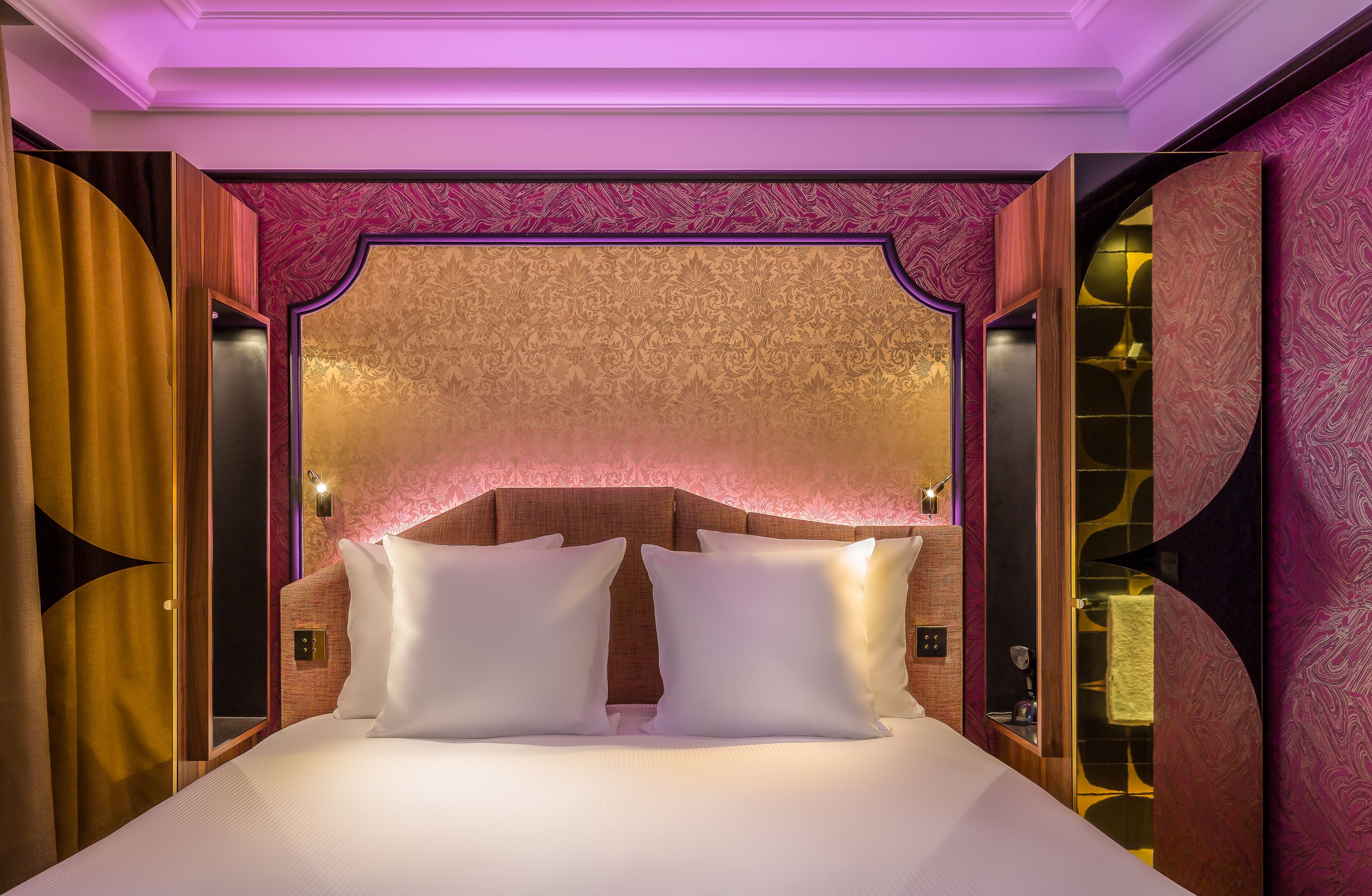 A luxurious hotel room with a large bed, ornate headboard, and a mirror.