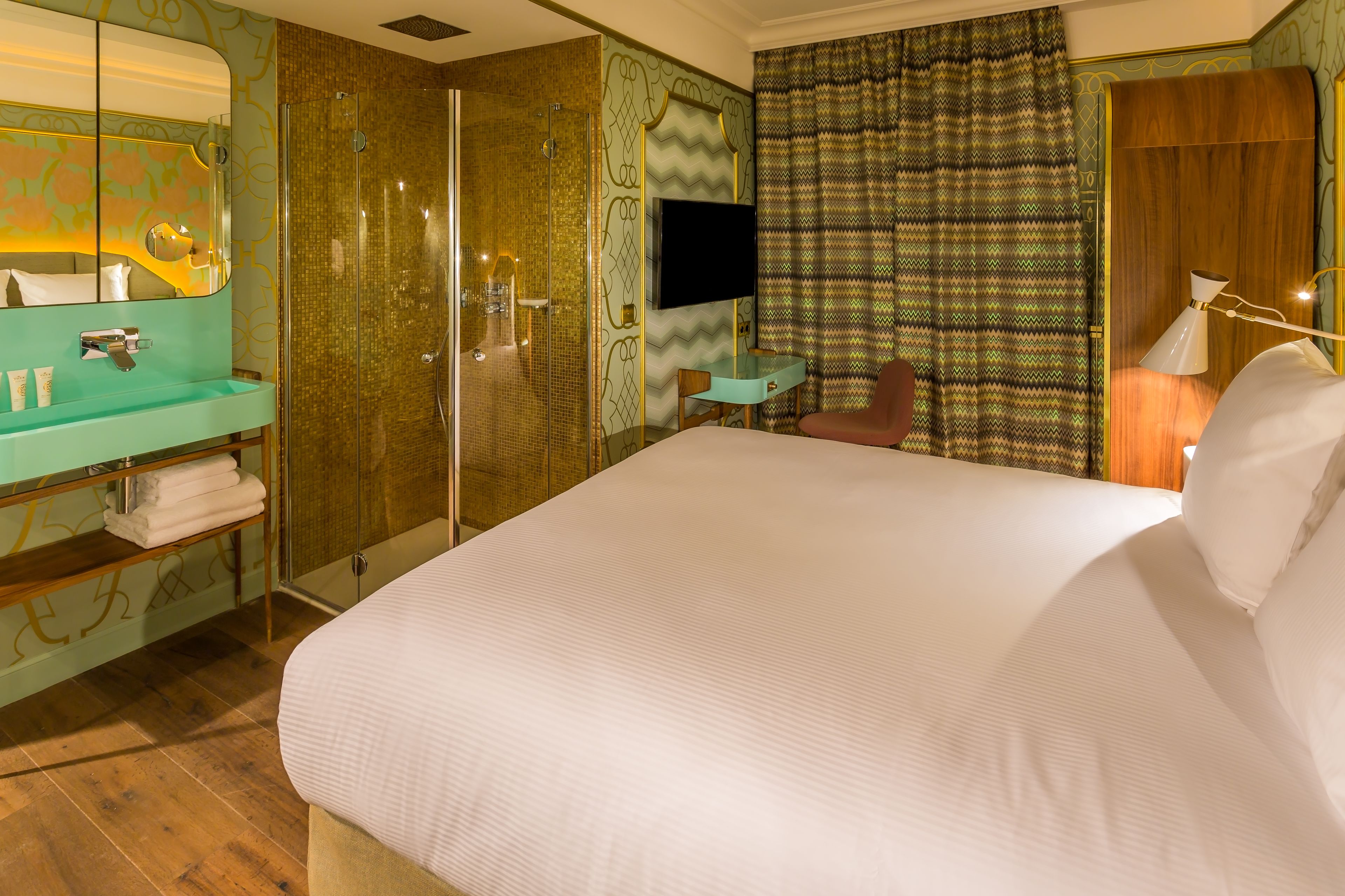 A hotel room with a large bed, a bathroom with a mirror and sink, a TV, and a patterned curtain.