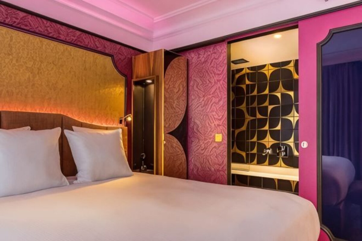 Une chambre d’hôtel avec un lit, une tête de lit en bois, un mur orné de motifs circulaires et une porte au motif géométrique.