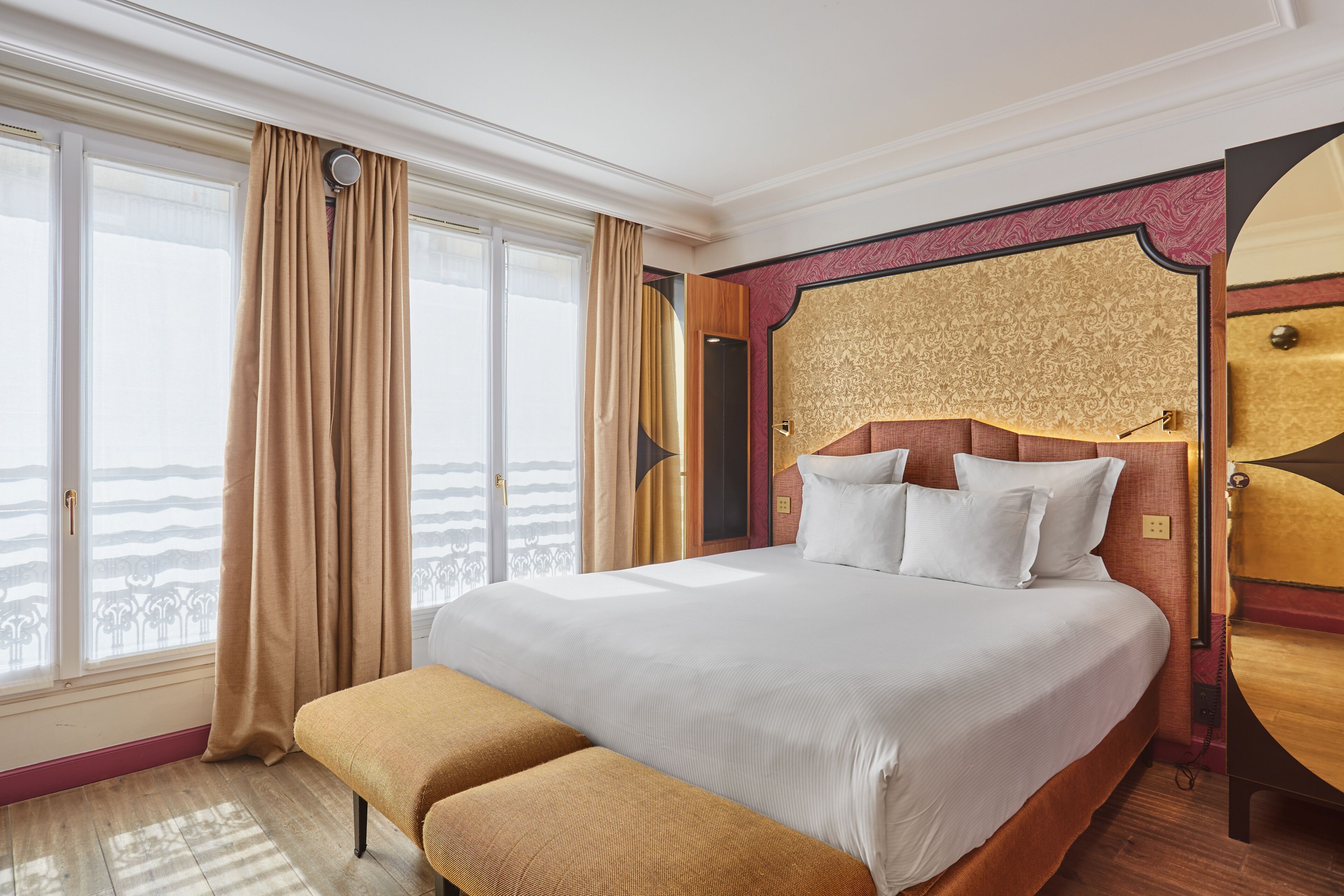 A large bed with white linens, a bench, and a view of the sea through large windows.