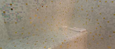 Une zone de douche carrelée avec un banc et une serviette.