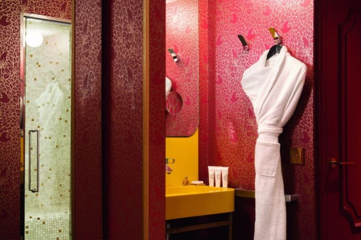 Ein Badezimmer mit Duschkabine aus Glas, einem gelben Waschbecken und einem weißen Bademantel, der an einem Haken hängt.